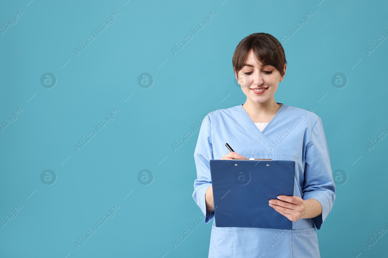 Photo of Portrait of smiling medical assistant with clipboard on light blue background. Space for text