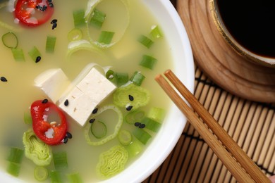 Photo of Bowl of delicious miso soup with tofu and chopsticks served on bamboo mat, top view