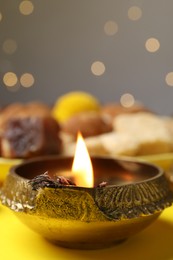 Happy Diwali. Diya lamp on yellow table against blurred lights, closeup. Space for text