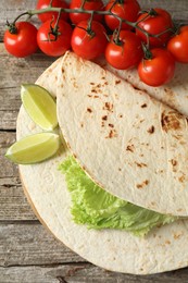 Photo of Tasty homemade tortillas, tomatoes, lime and lettuce on wooden table, top view