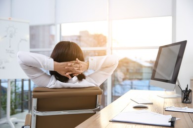 Woman relaxing in office chair at workplace, back view