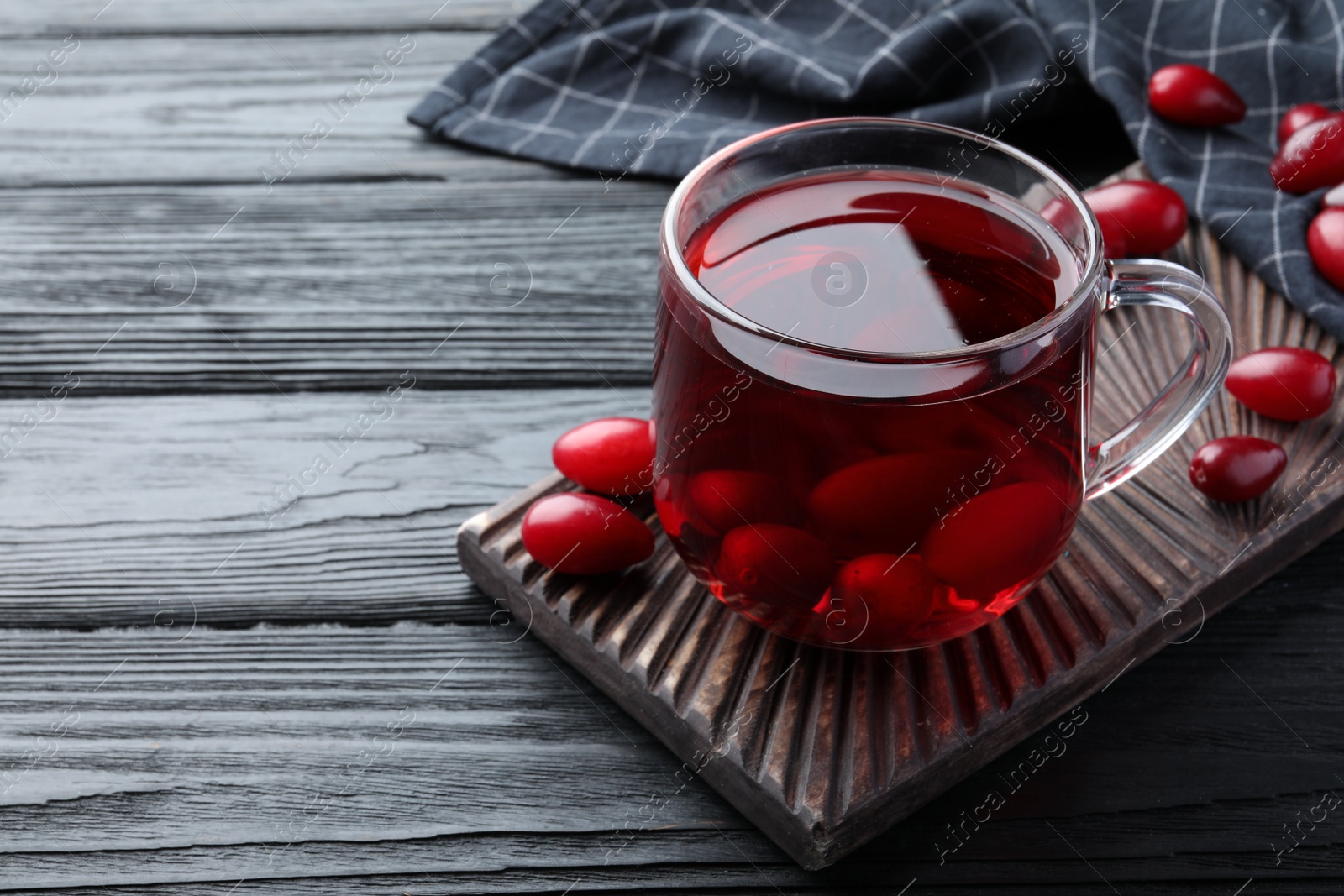 Photo of Glass cup of fresh dogwood tea with berries on black wooden table. Space for text