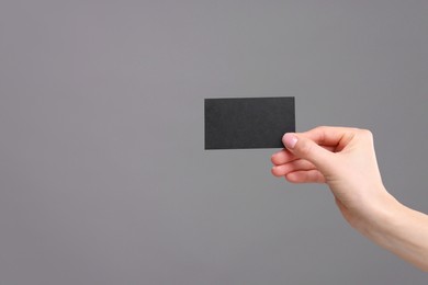 Woman holding blank business card on grey background, closeup. Space for text