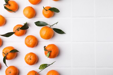 Photo of Fresh ripe tangerines with green leaves on white table, flat lay. Space for text