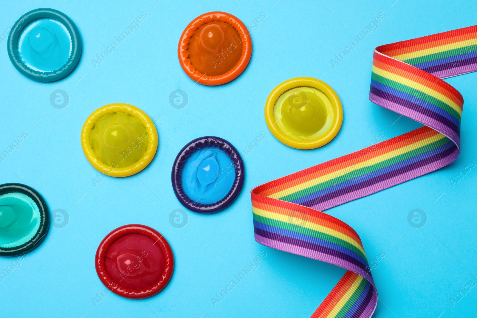 Photo of Colorful condoms and rainbow ribbon on light blue background, flat lay. LGBT concept