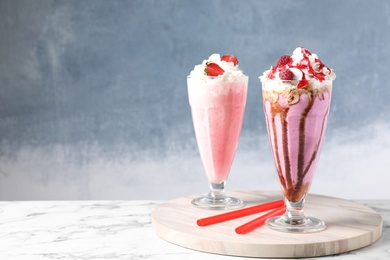 Photo of Tasty milk shakes with toppings on white marble table against blue background. Space for text