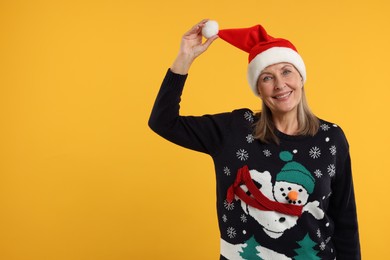 Photo of Happy senior woman in Christmas sweater and Santa hat on orange background. Space for text