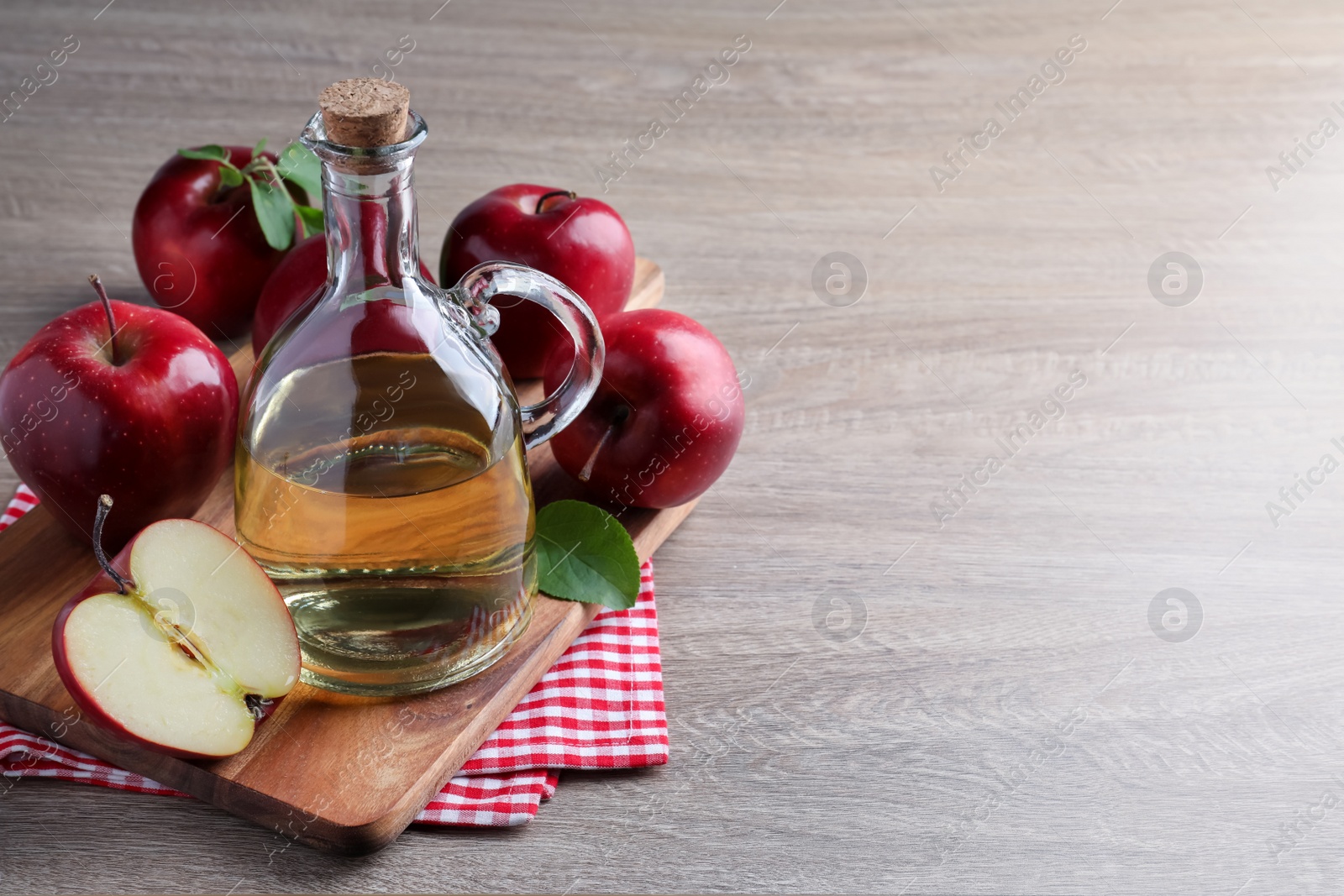 Photo of Jug of tasty juice and fresh ripe red apples on wooden table, space for text