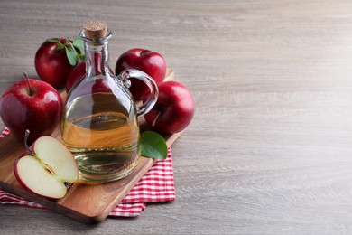 Photo of Jug of tasty juice and fresh ripe red apples on wooden table, space for text