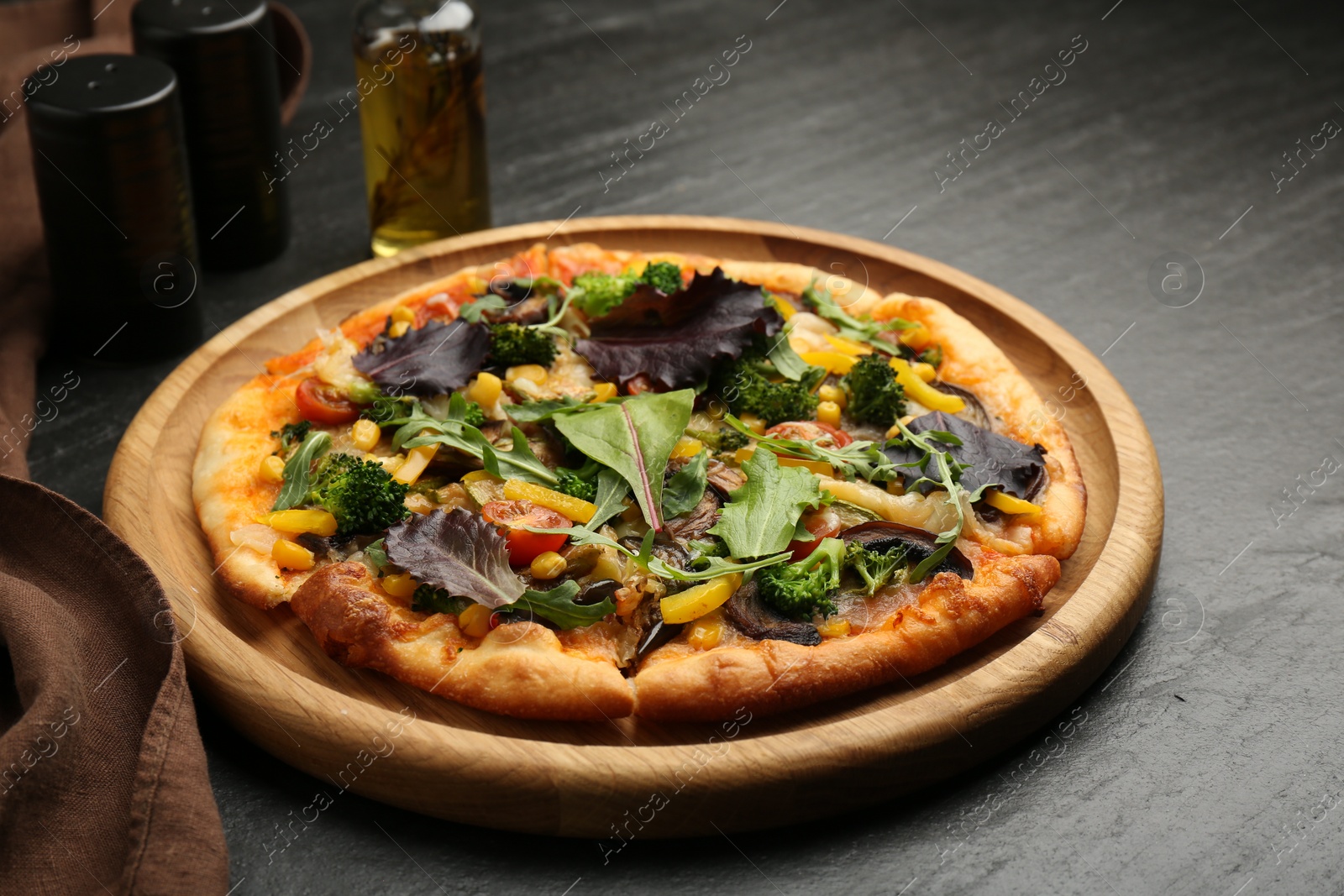 Photo of Delicious vegetarian pizza with mushrooms, vegetables and greens on black table