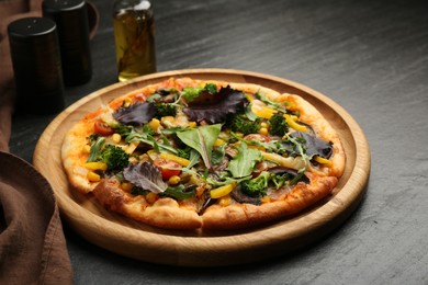 Photo of Delicious vegetarian pizza with mushrooms, vegetables and greens on black table