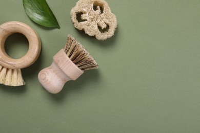 Photo of Cleaning brushes, loofah and leaf on green background, flat lay. Space for text