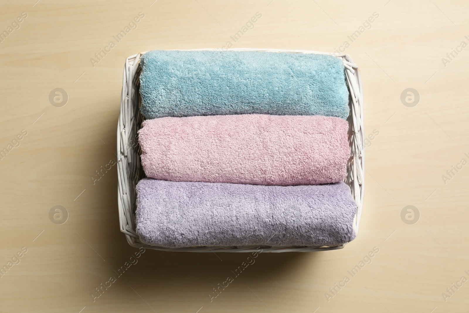 Photo of Wicker basket with clean soft towels on wooden table, top view