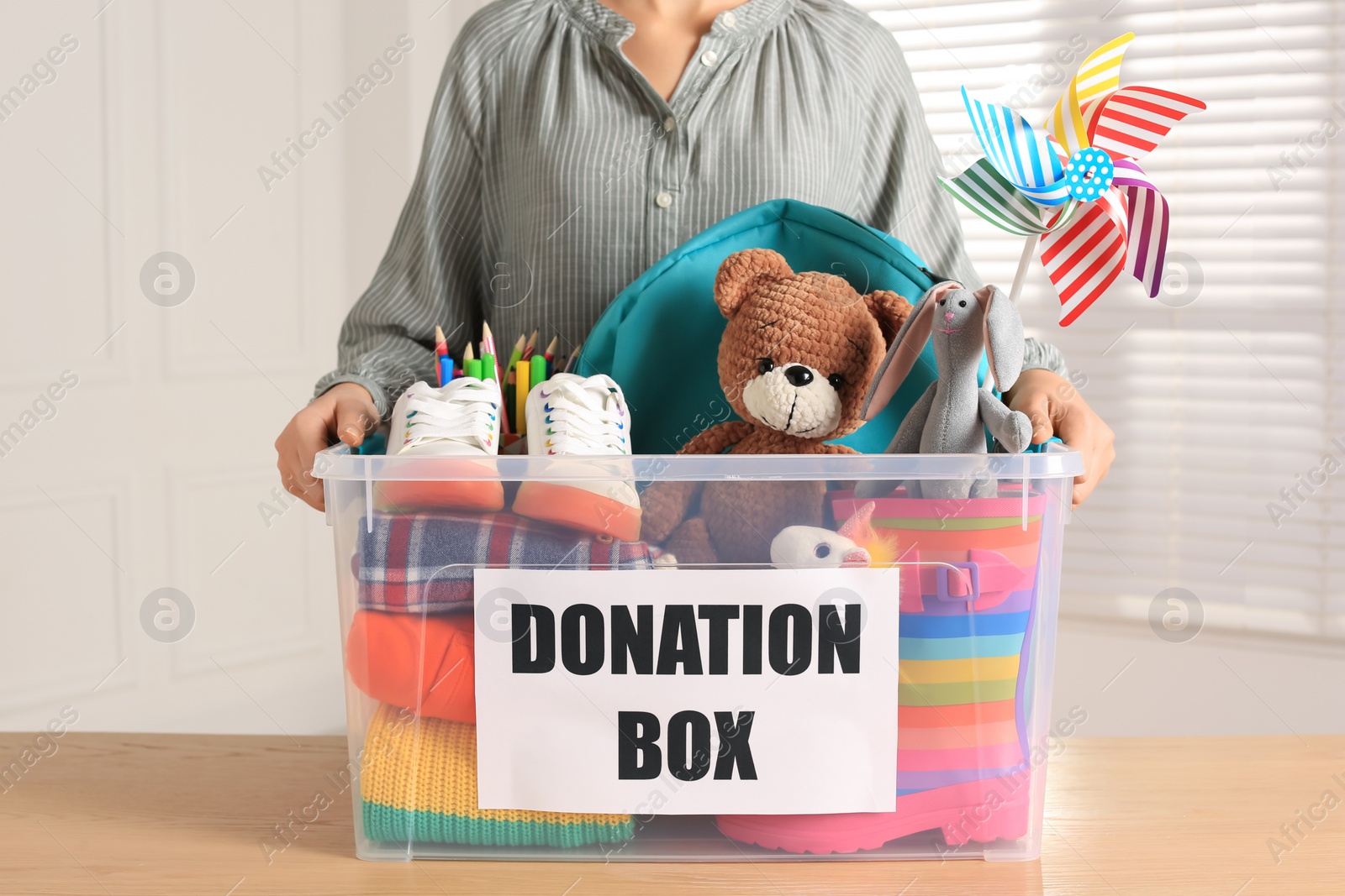 Photo of Woman holding donation box with child goods indoors, closeup