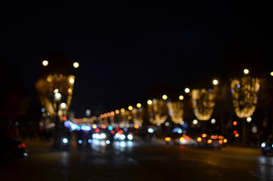 Blurred view of street with beautiful lights on trees and cars at night. Bokeh effect