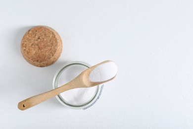 Photo of Baking soda in jar and spoon on white background, top view. Space for text