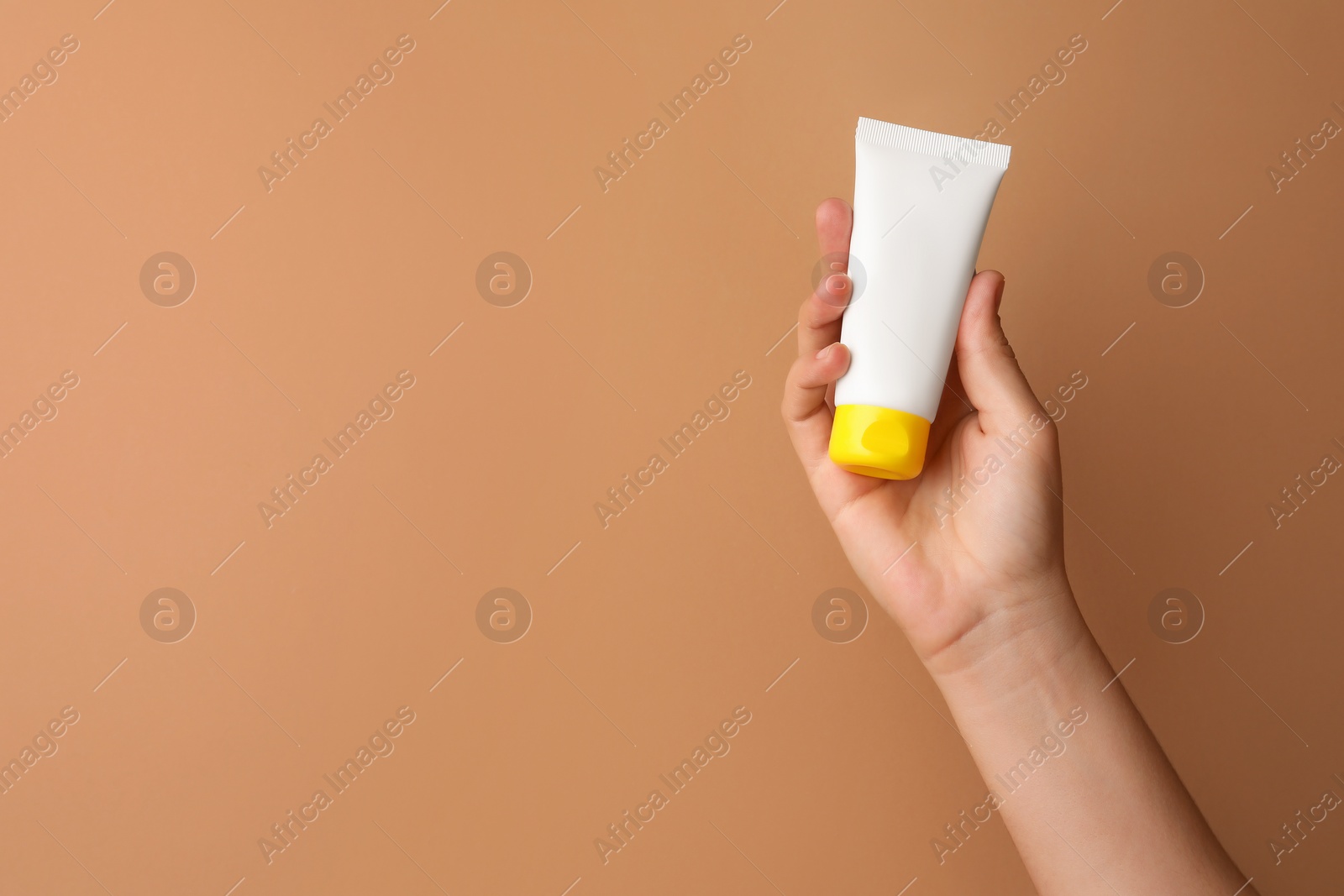 Photo of Woman holding tube of face cream on beige background, closeup. Space for text