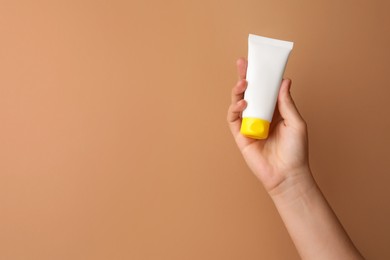 Woman holding tube of face cream on beige background, closeup. Space for text