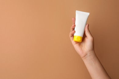 Photo of Woman holding tube of face cream on beige background, closeup. Space for text