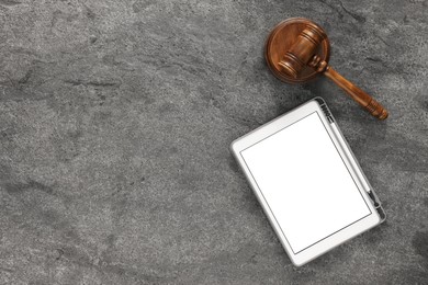 Modern tablet and gavel on gray textured table, flat lay. Space for text