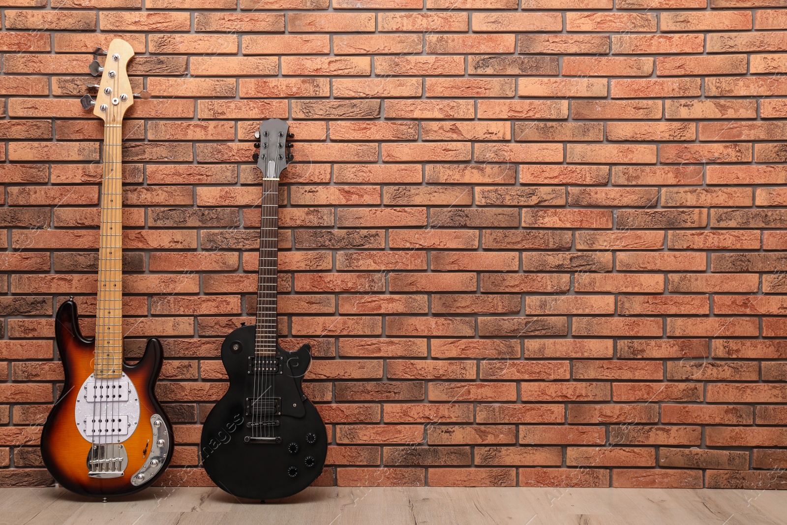 Photo of Modern electric guitars near red brick wall indoors. Space for text