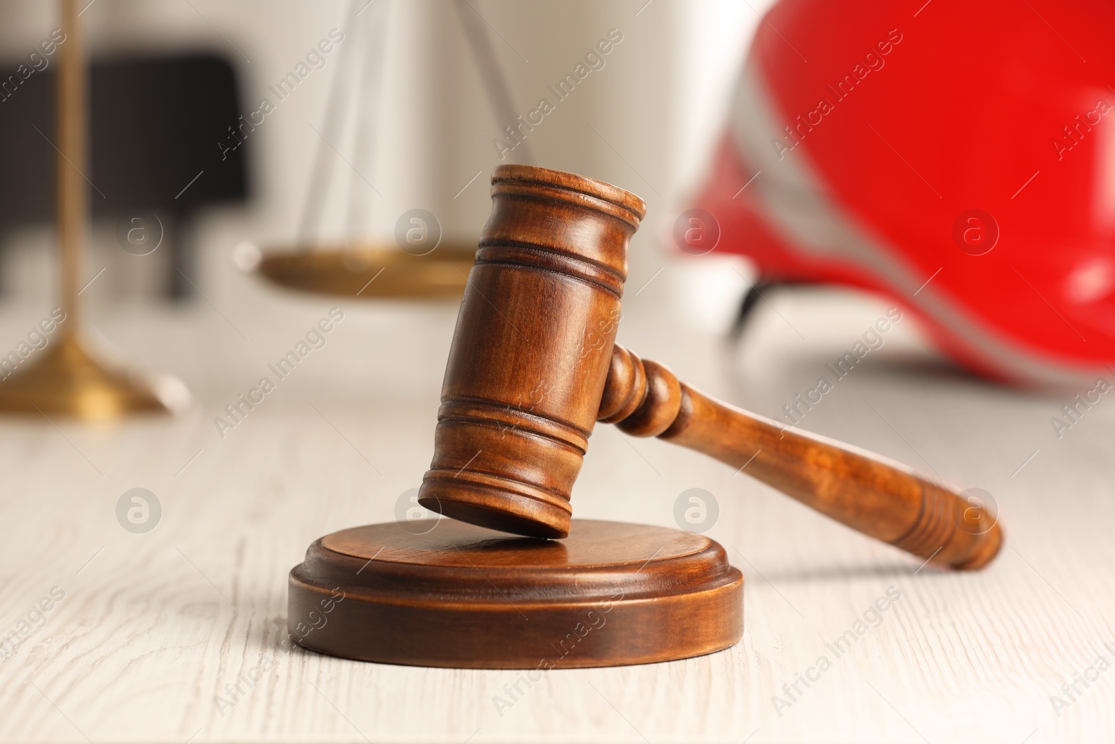 Photo of Law concept. Gavel, scales and red hard hat on white wooden table, closeup