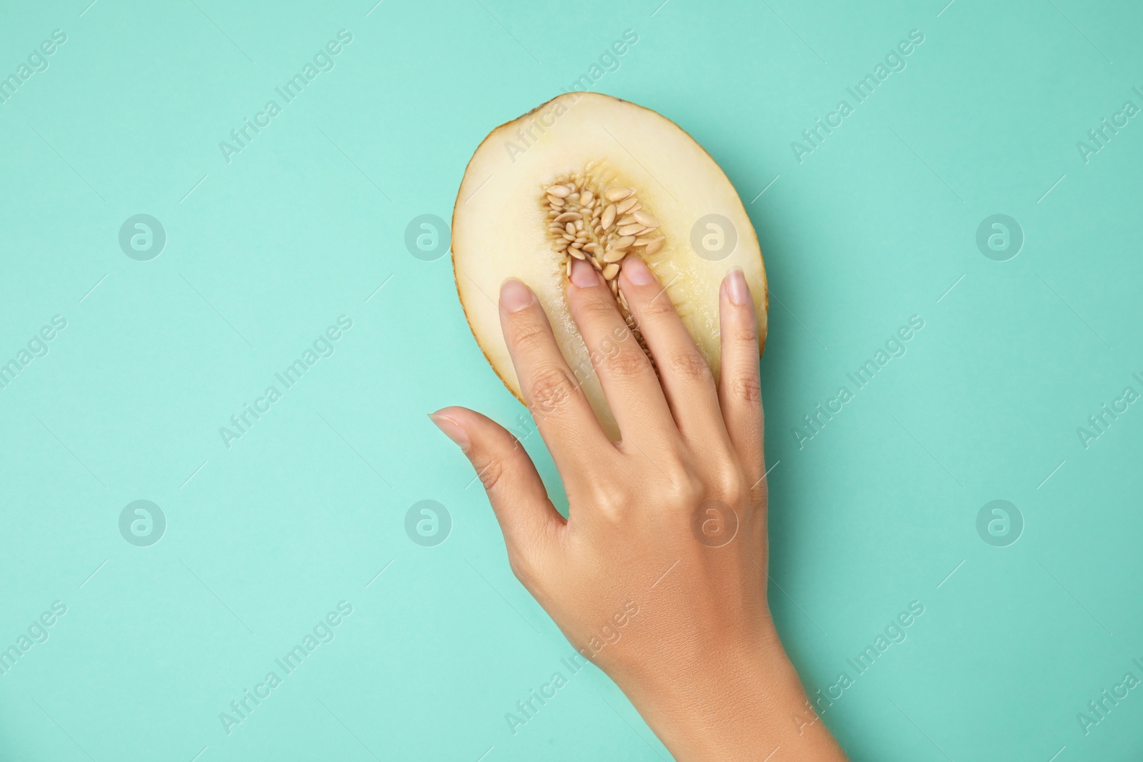Photo of Young woman touching half of melon on turquoise background, top view. Sex concept