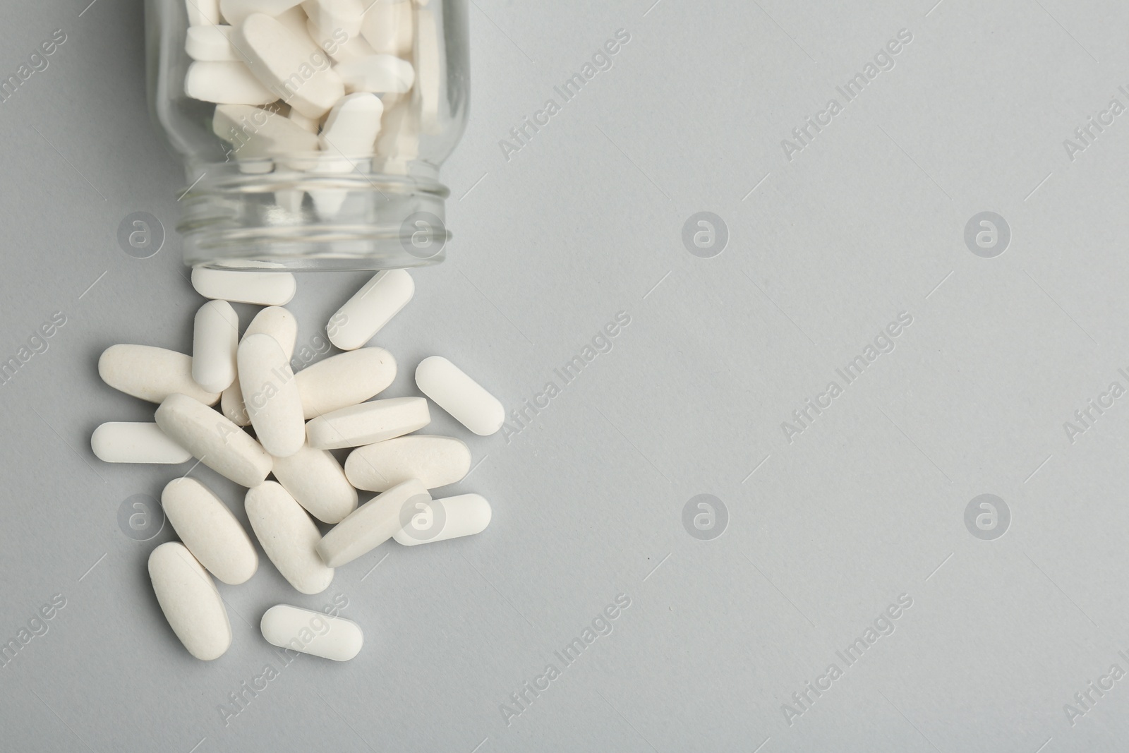 Photo of Vitamin pills and bottle on grey background, top view. Space for text