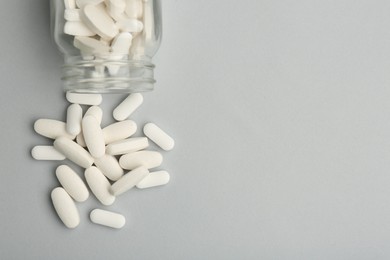 Photo of Vitamin pills and bottle on grey background, top view. Space for text