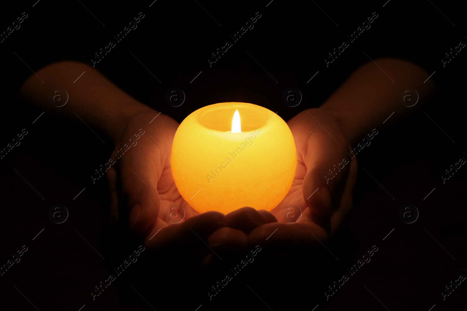 Photo of Woman holding burning candle in hands on black background, closeup