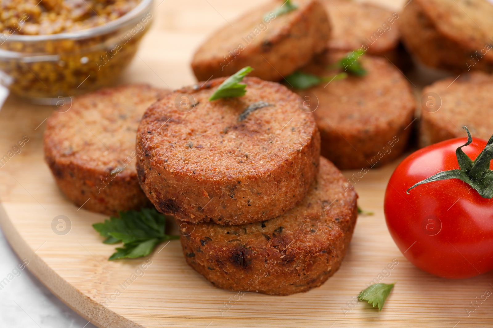 Photo of Tasty vegan cutlets and tomato on wooden board, closeup