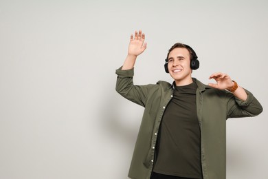 Handsome young man with headphones dancing on light grey background. Space for text