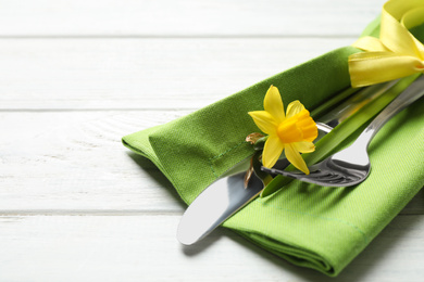 Photo of Cutlery set with beautiful narcissus on white wooden table, closeup. Easter celebration