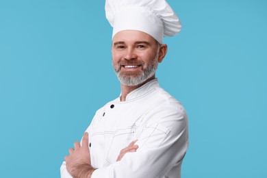 Photo of Happy chef in uniform on light blue background