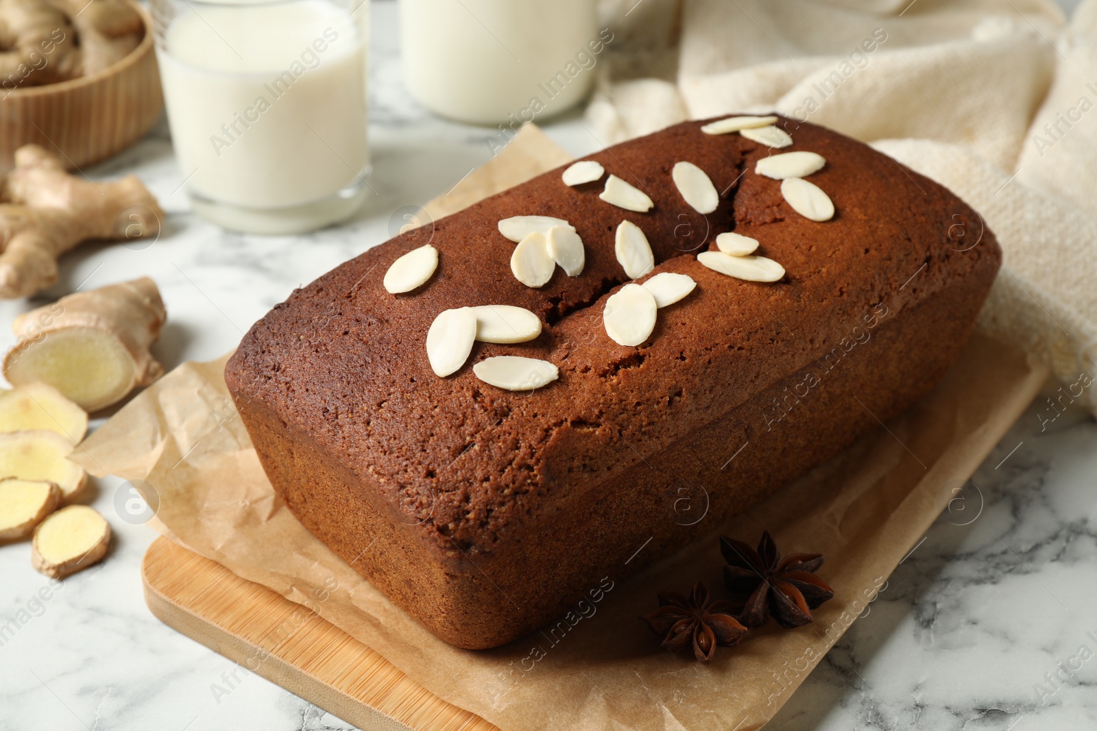 Photo of Delicious gingerbread cake with almond petals on white marble table