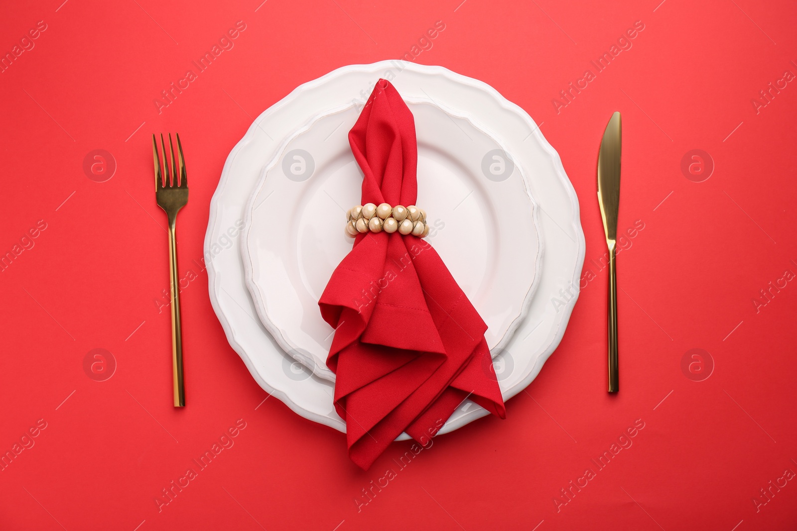 Photo of Place setting with napkin on red table, top view