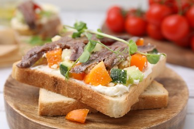 Delicious toasts with anchovies, cream cheese, bell peppers and cucumbers on white table, closeup