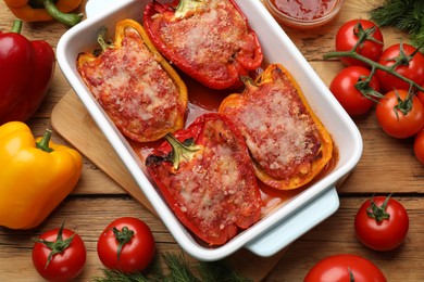 Photo of Tasty stuffed peppers in dish and ingredients on wooden table, flat lay