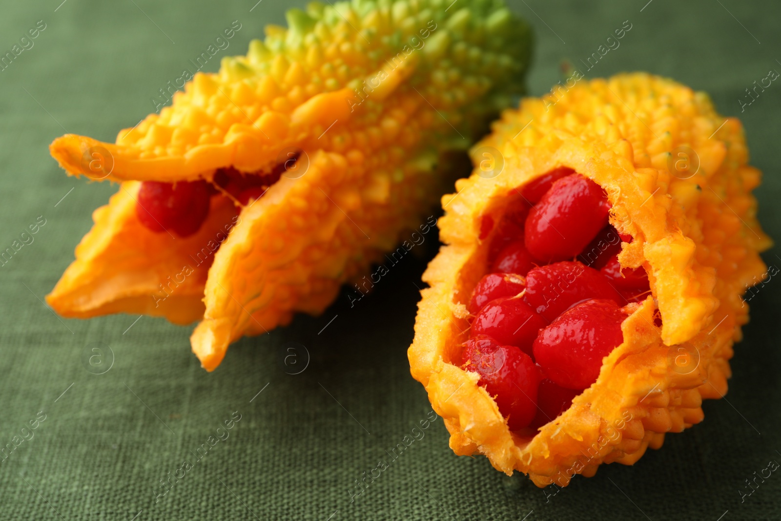 Photo of Fresh bitter melons with red seeds on dark green cloth, closeup