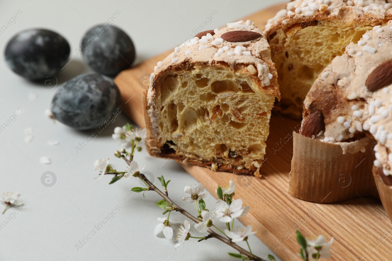 Photo of Pieces of delicious Italian Easter dove cake (traditional Colomba di Pasqua), branch with flowers and painted eggs on light grey table, closeup