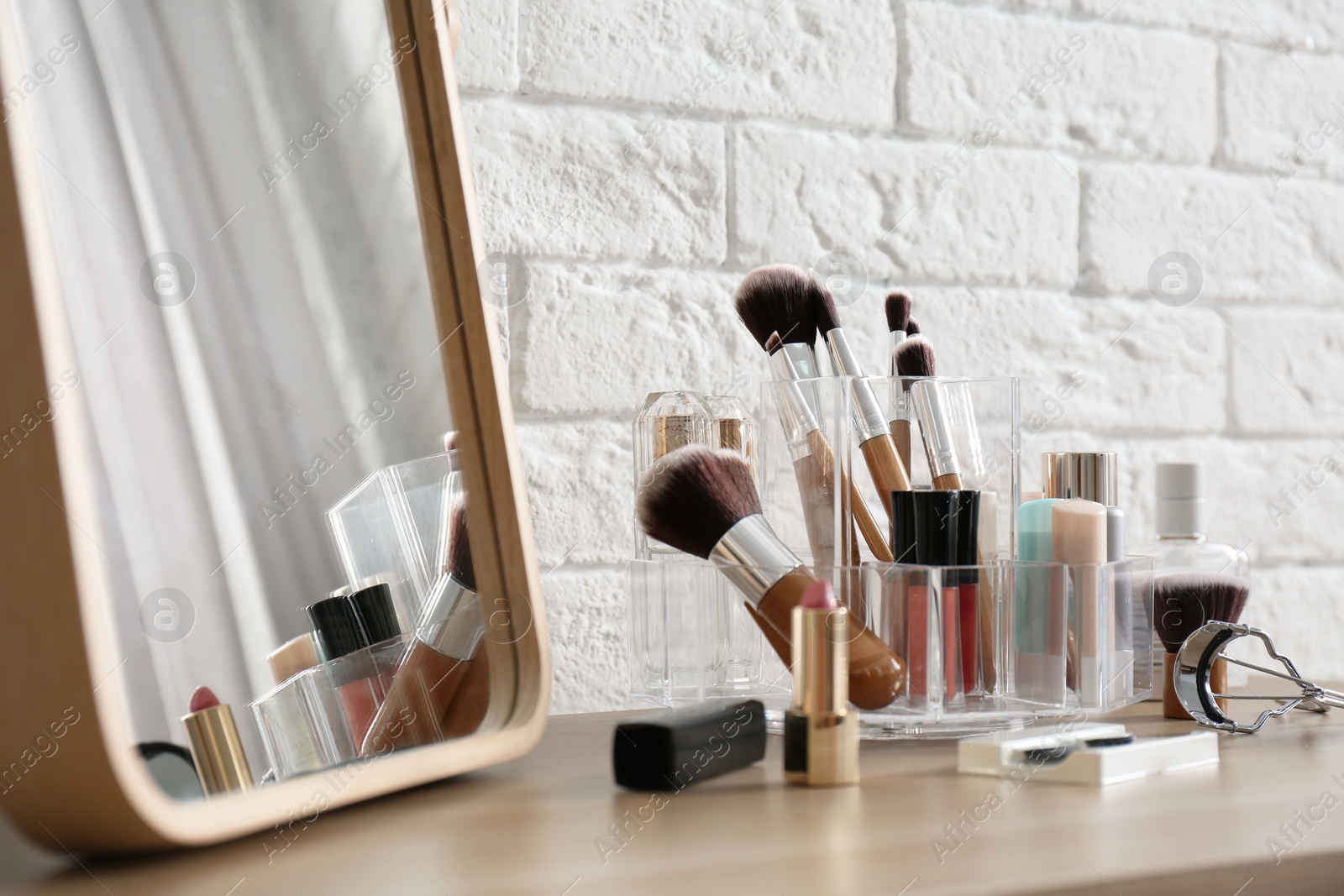 Photo of Organizer with cosmetic products for makeup on table near brick wall