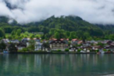 Photo of Blurred view of beautiful village on lake shore near mountains