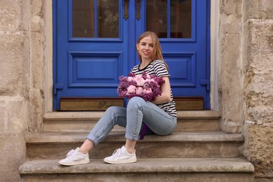 Photo of Beautiful woman with bouquet of spring flowers on stairs near building