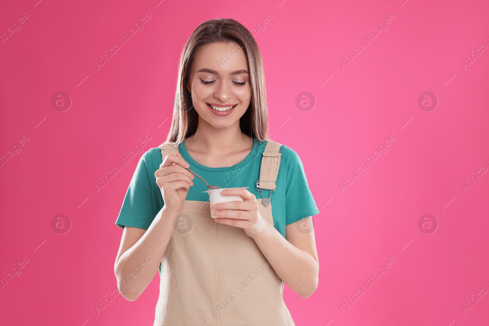 Photo of Young attractive woman with tasty yogurt on pink background