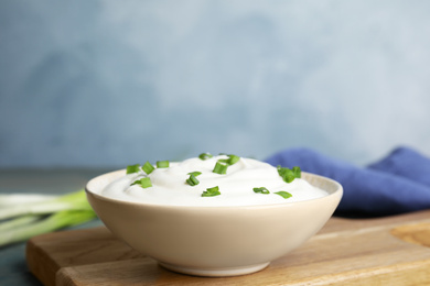 Photo of Fresh sour cream with onion on wooden board against light blue background, closeup