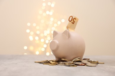 Photo of Piggy bank with euro banknote and coins on grey table against blurred lights, space for text