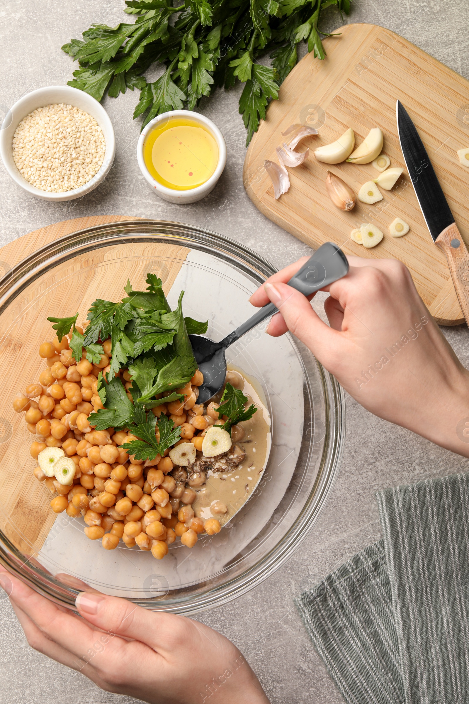 Photo of Woman mixing ingredients for delicious hummus at light grey table, top view