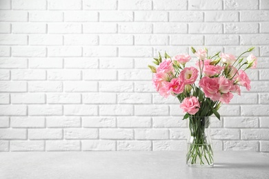 Photo of Eustoma flowers in vase on table near white brick wall, space for text