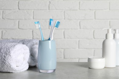 Plastic toothbrushes in holder, cosmetic products and towels on light grey table. Space for text