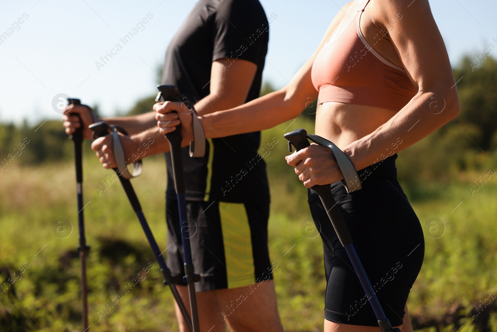 Photo of Couple practicing Nordic walking with poles outdoors on sunny day, closeup